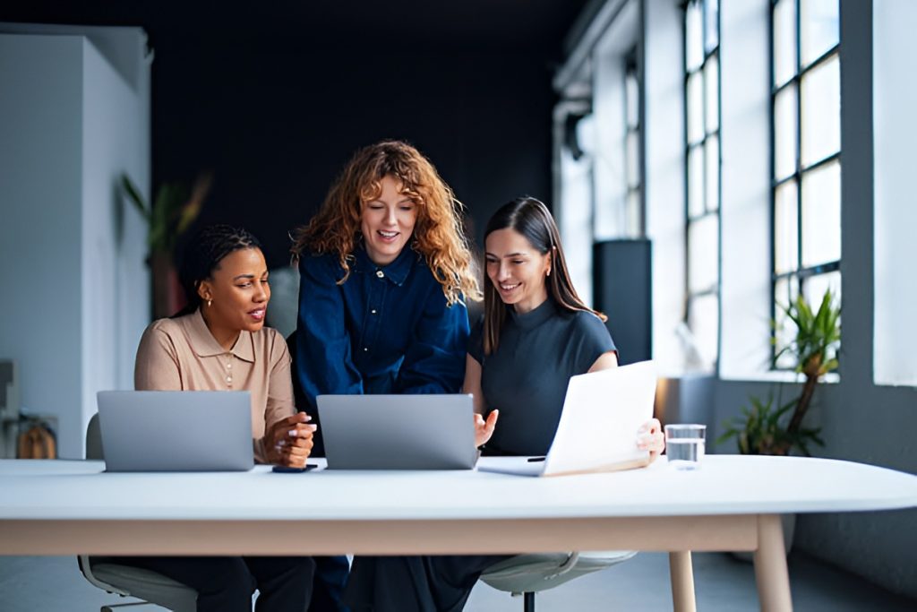 three female office workers using laptops while collaborating